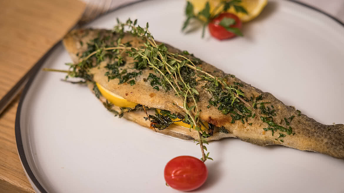 Gebratene Forelle auf einem Teller mit Zitrone, Petersilie und Kirschtomate dekoriert